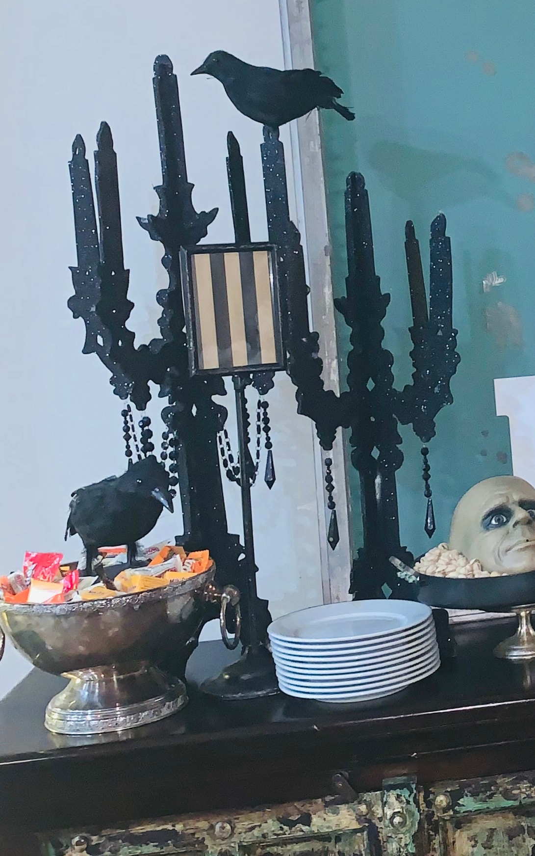 Halloween candelabra display with black crow, skull, and candy bowl on dark sideboard