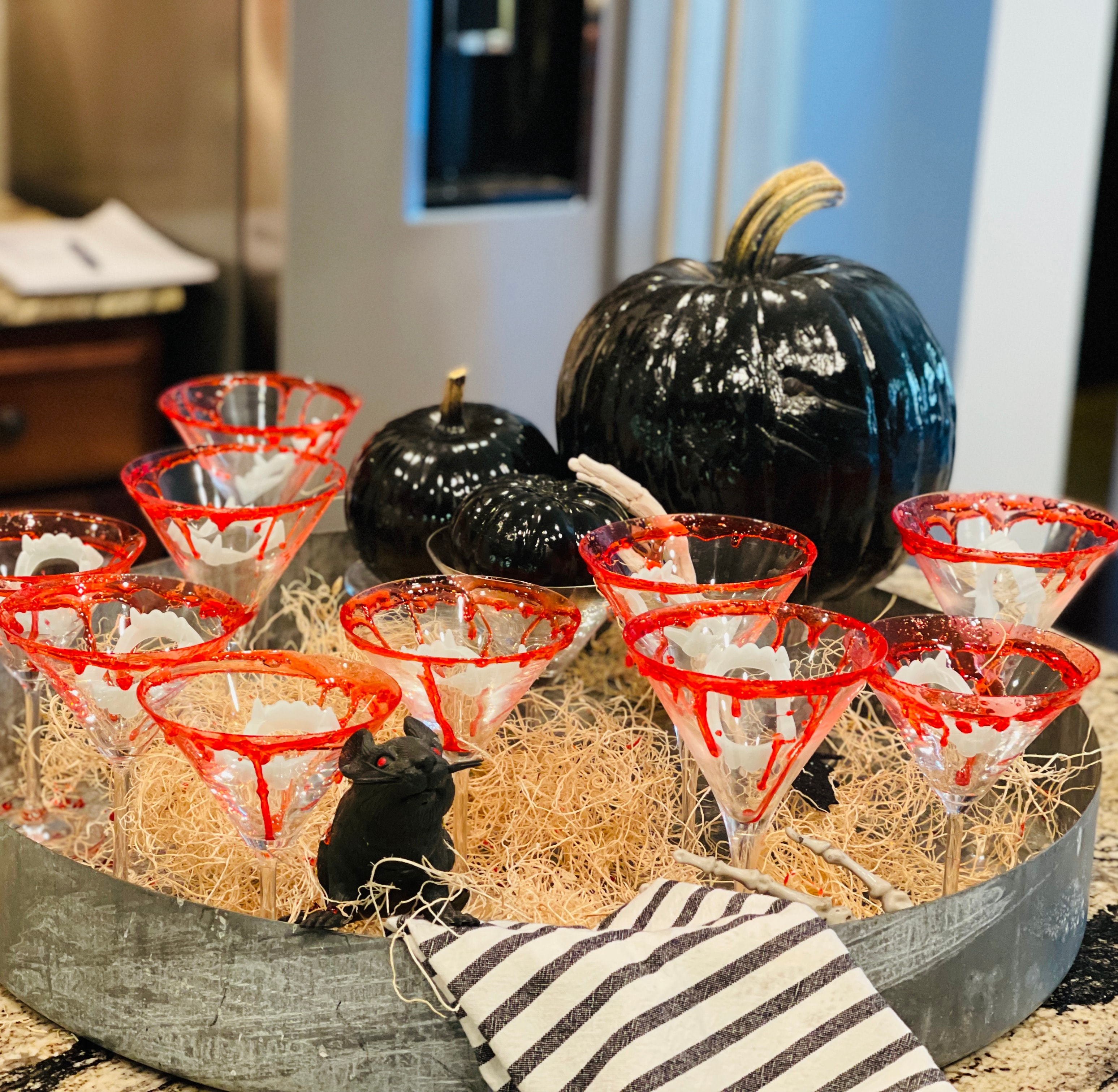 Halloween martini glass display with black pumpkins and red-rimmed glasses on a galvanized tray