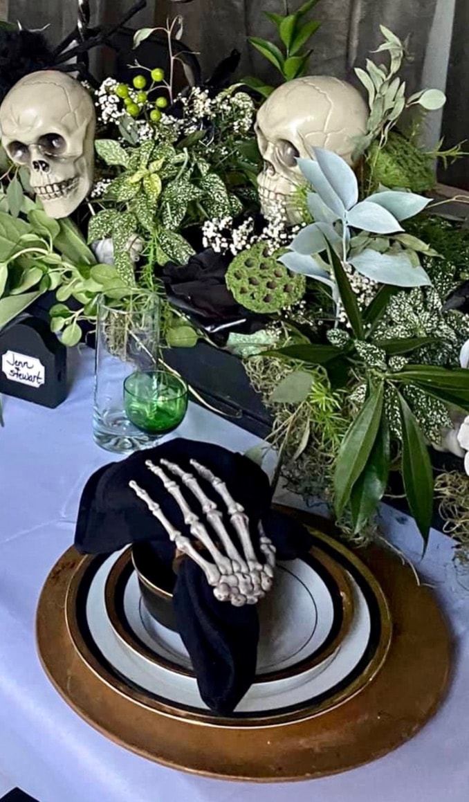 Halloween tablescape with skull centerpieces, black napkins, and botanical greenery