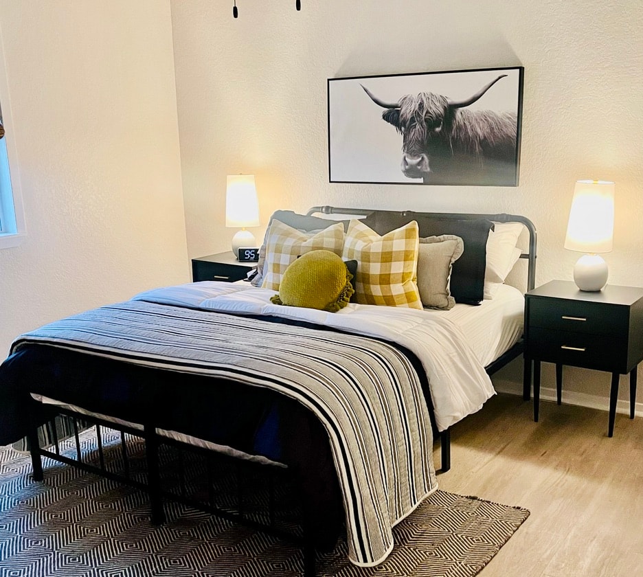 Modern bedroom with black iron bed, highland cow art, and mustard plaid pillows