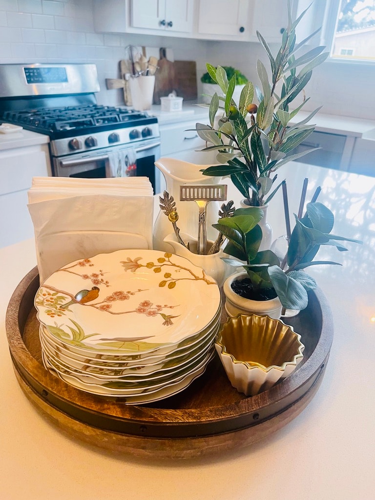 Kitchen counter styled with bird-print plates, olive branch, and gold accents on a wood tray