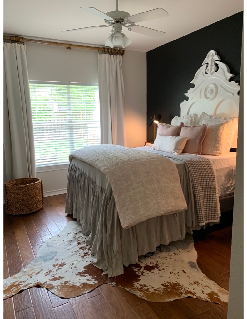 Romantic bedroom with ornate white headboard, cowhide rug, and dark accent wall